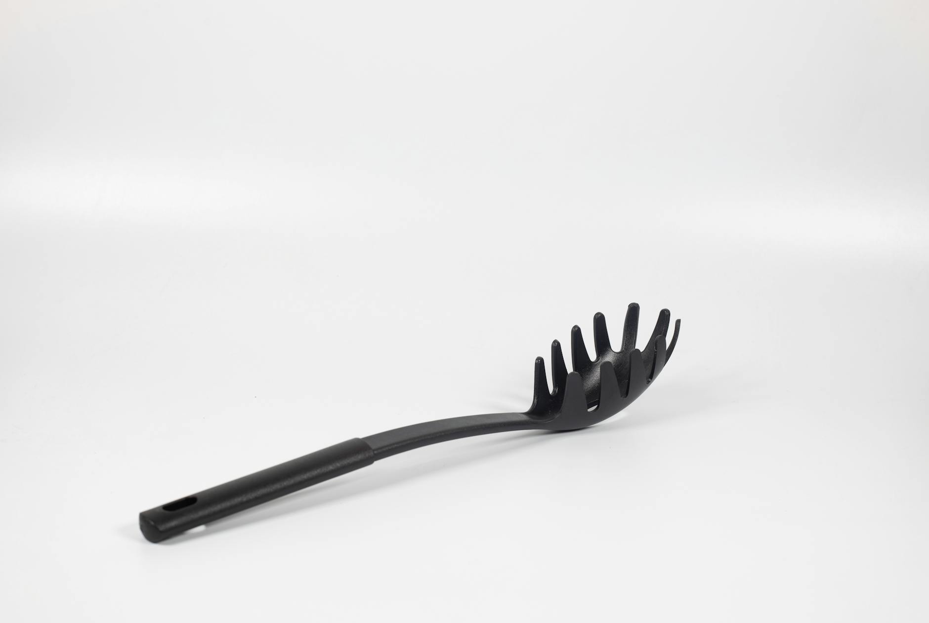 A black plastic pasta server isolated on a white background, ideal for kitchen use.