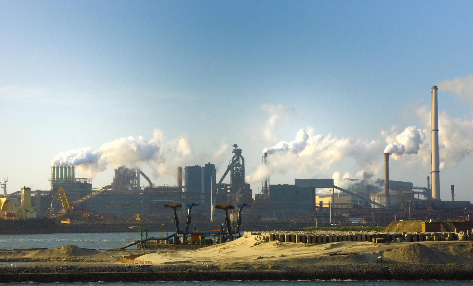 View of the steel plant in IJmuiden, Netherlands with smoke pollution against a clear sky.