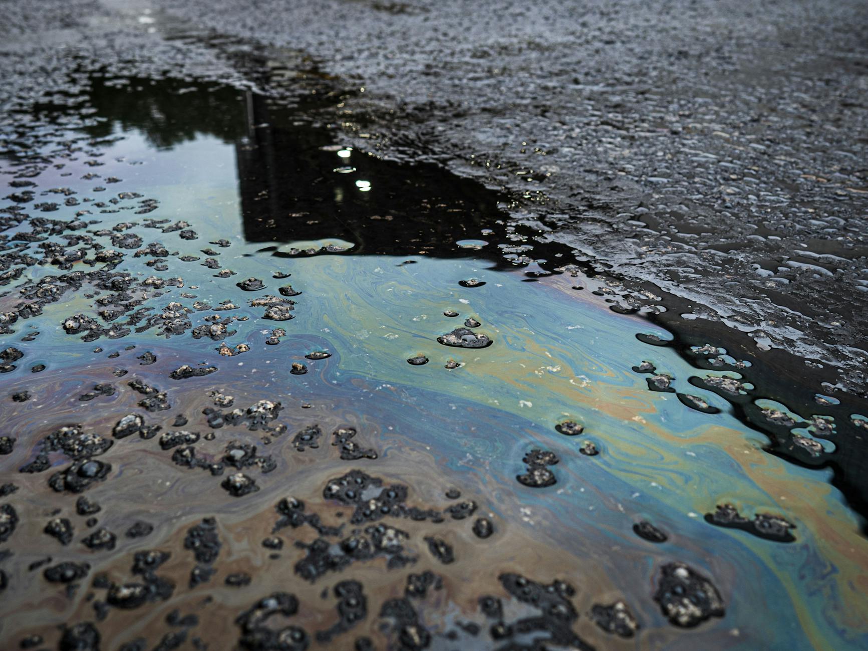 A vivid iridescent oil spill on rough asphalt surface, highlighting environmental contamination.