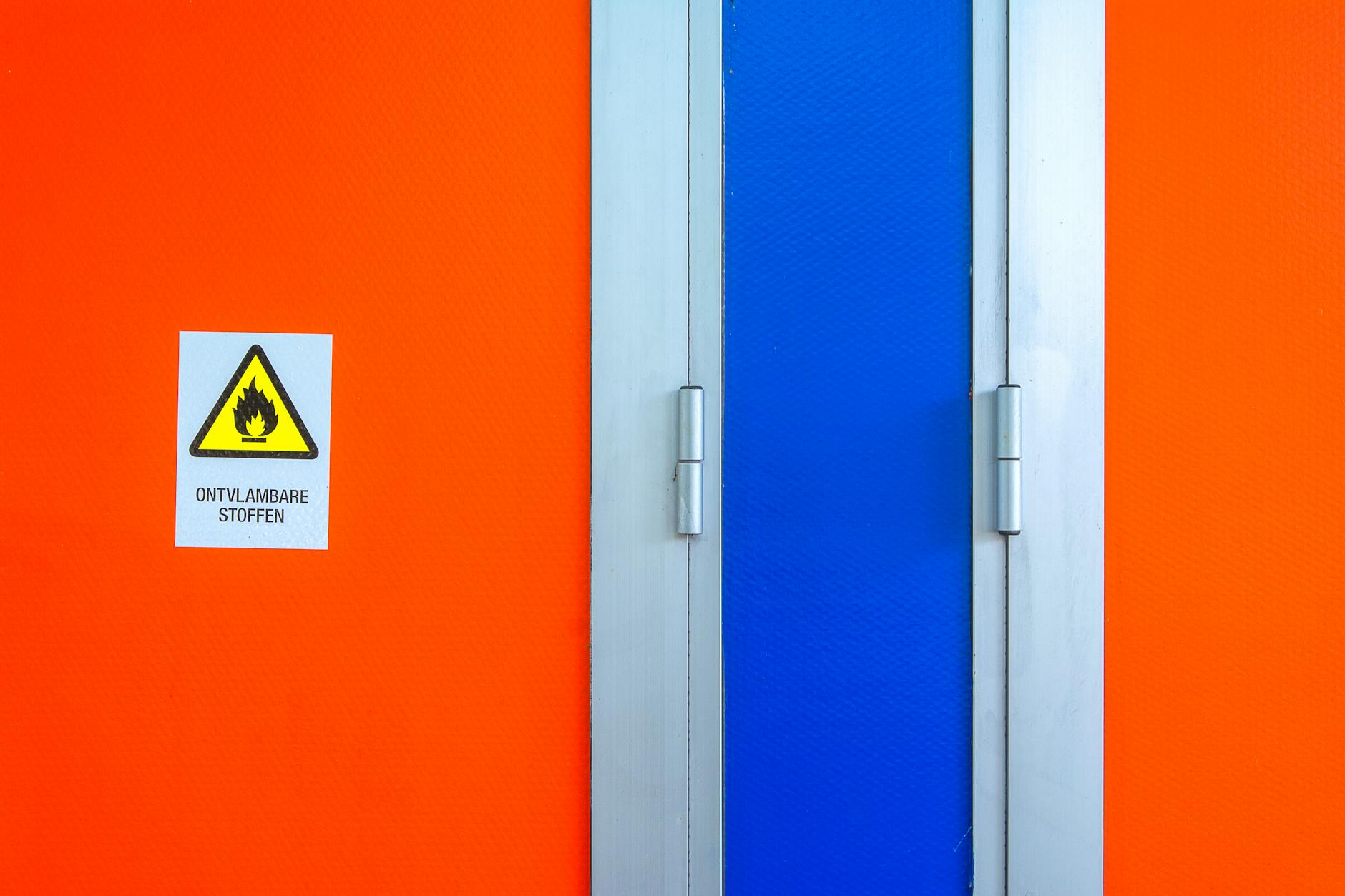 Bright orange wall with a blue door displaying a flammable materials warning sign.