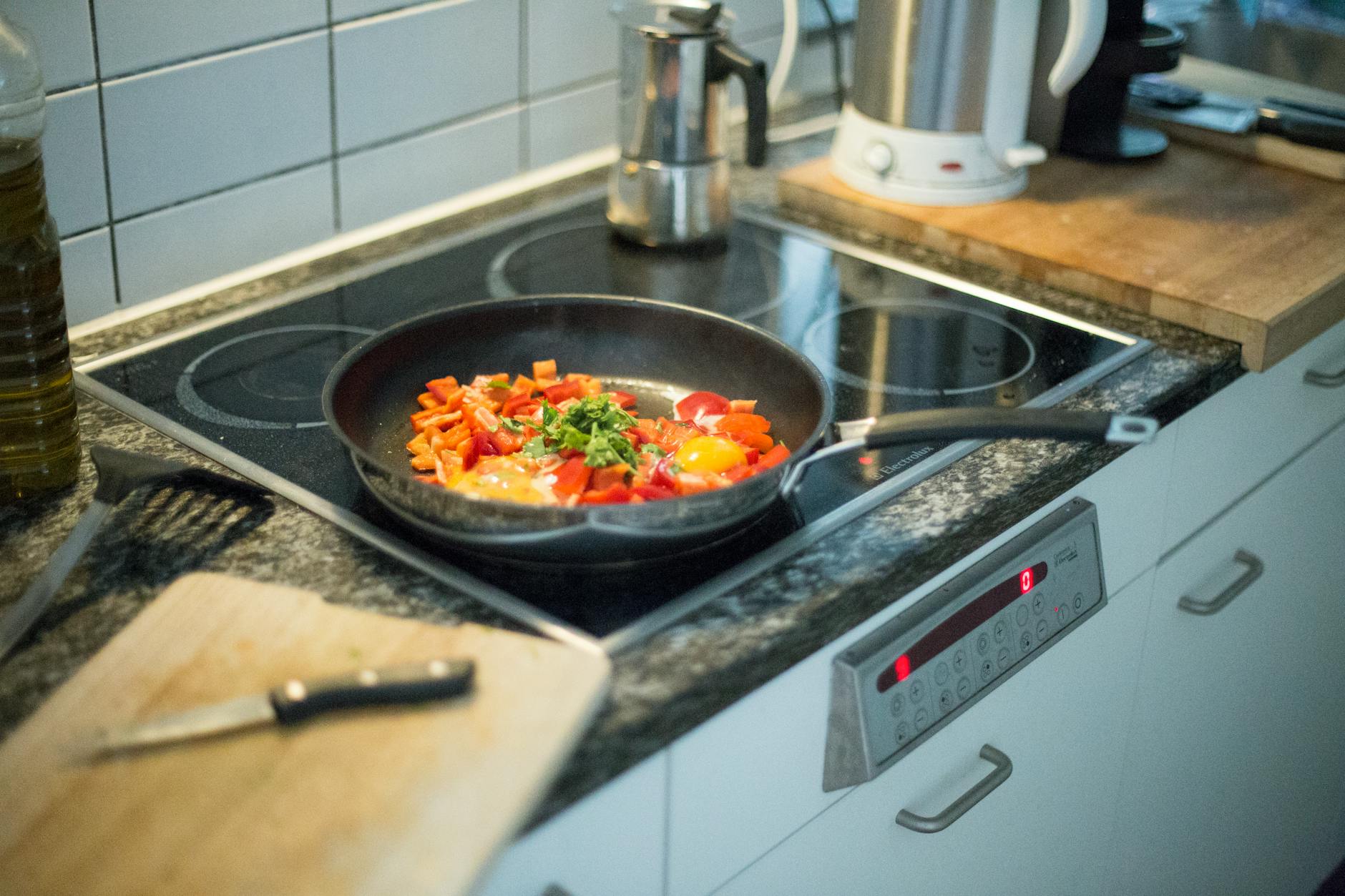 A colorful pan with eggs and vegetables cooking on an electric stove in a modern kitchen setting.
