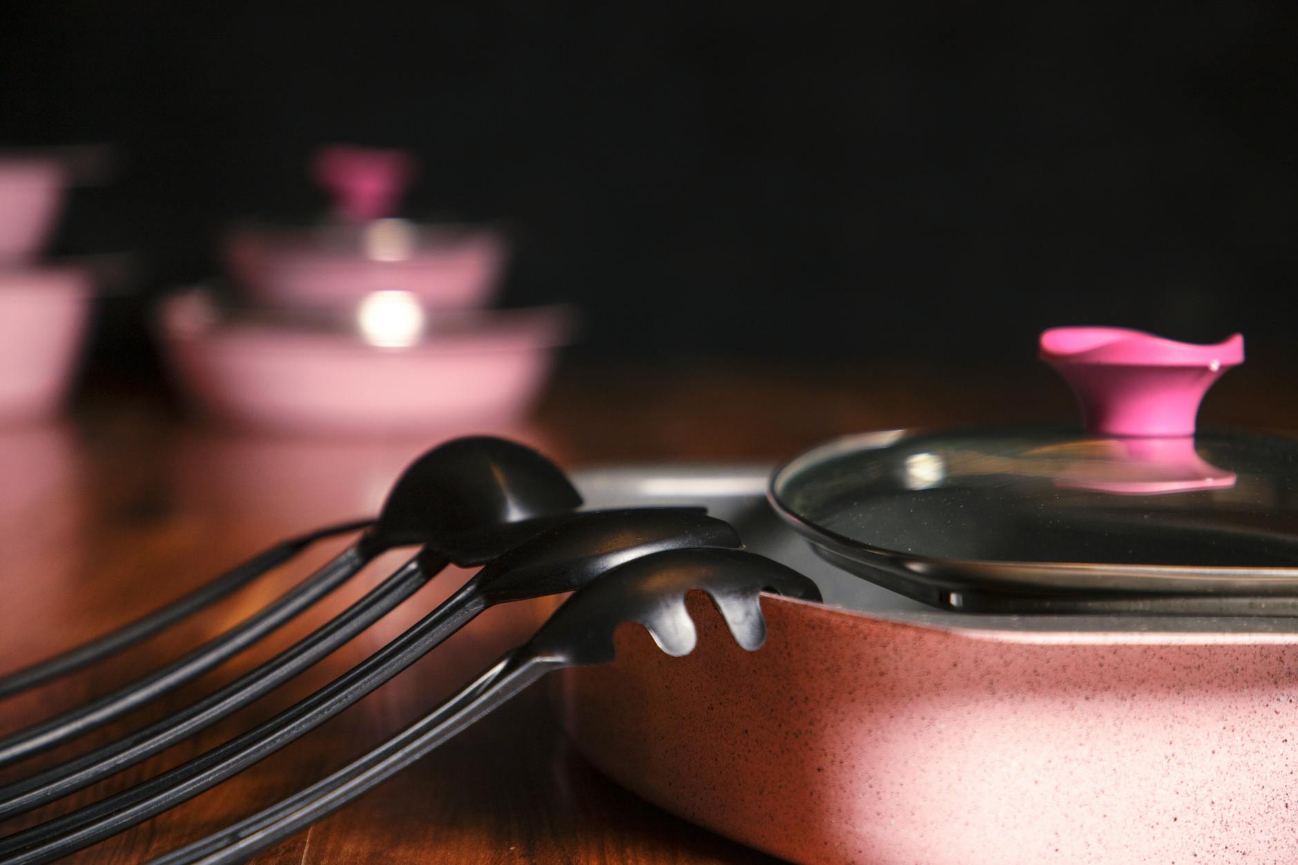 Close-up of pink cookware and utensils on a wooden countertop, emphasizing elegance and style.