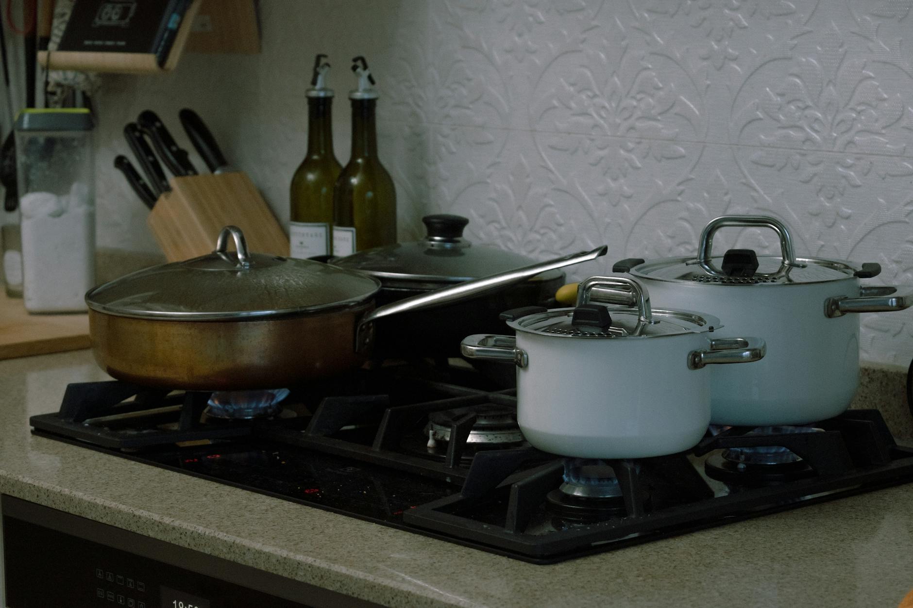 A home kitchen scene featuring pots and pans on a gas stove, showcasing a warm cooking setting.