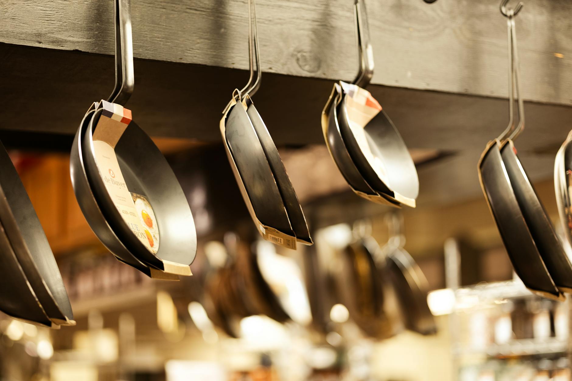 A selection of frying pans hanging in a kitchenware shop for sale.
